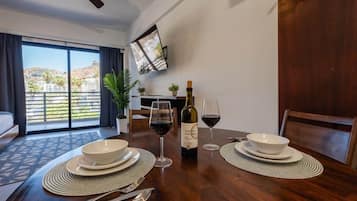 Een eethoek met een tafel gedekt voor twee personen, een fles wijn en een aan de muur bevestigde televisie.