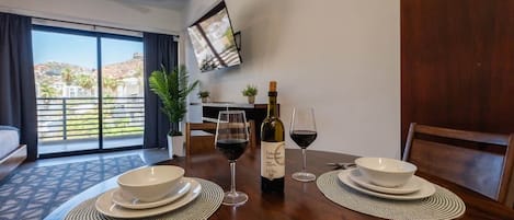 A dining area with a table set for two, a bottle of wine, and a TV mounted on the wall.