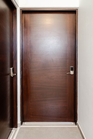 Eine geschlossene Holztür mit moderner Beschlagung, platziert in einer Ecke mit weißer Wand und Teppichboden.
