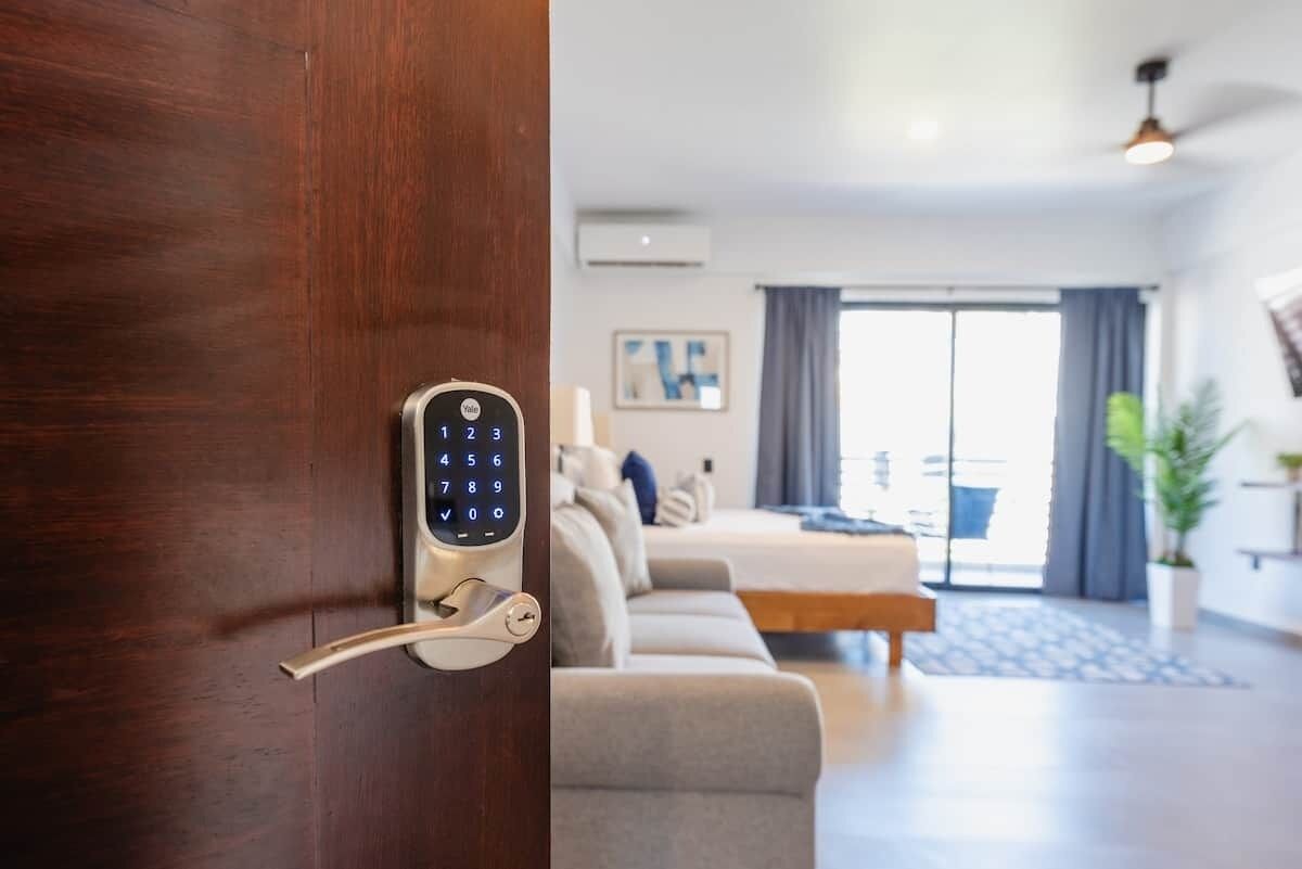 Une chambre d’hôtel moderne dotée d’une serrure à clavier numérique, d’un canapé, d’un lit et d’une grande fenêtre avec des rideaux.
