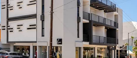 A modern building with a flat facade, multiple balconies, and a visible storefront with mannequins.