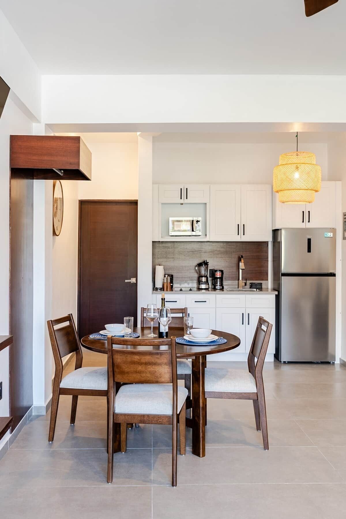 Une cuisine moderne avec des meubles blancs, un réfrigérateur en acier inoxydable et un coin repas comprenant une table et des chaises en bois.