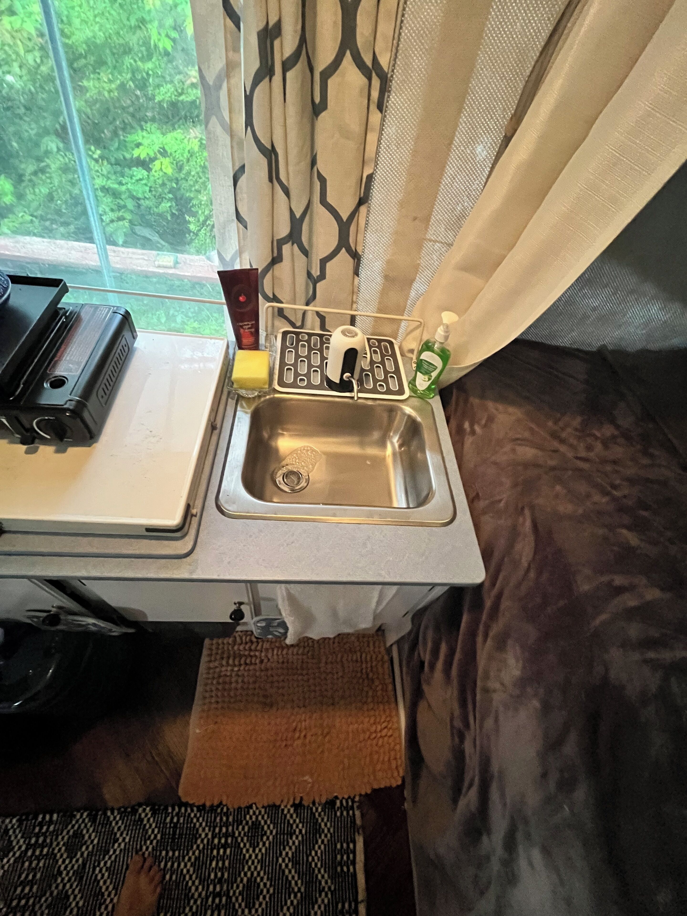 A compact kitchen with a sink, a radio, and a window with curtains.