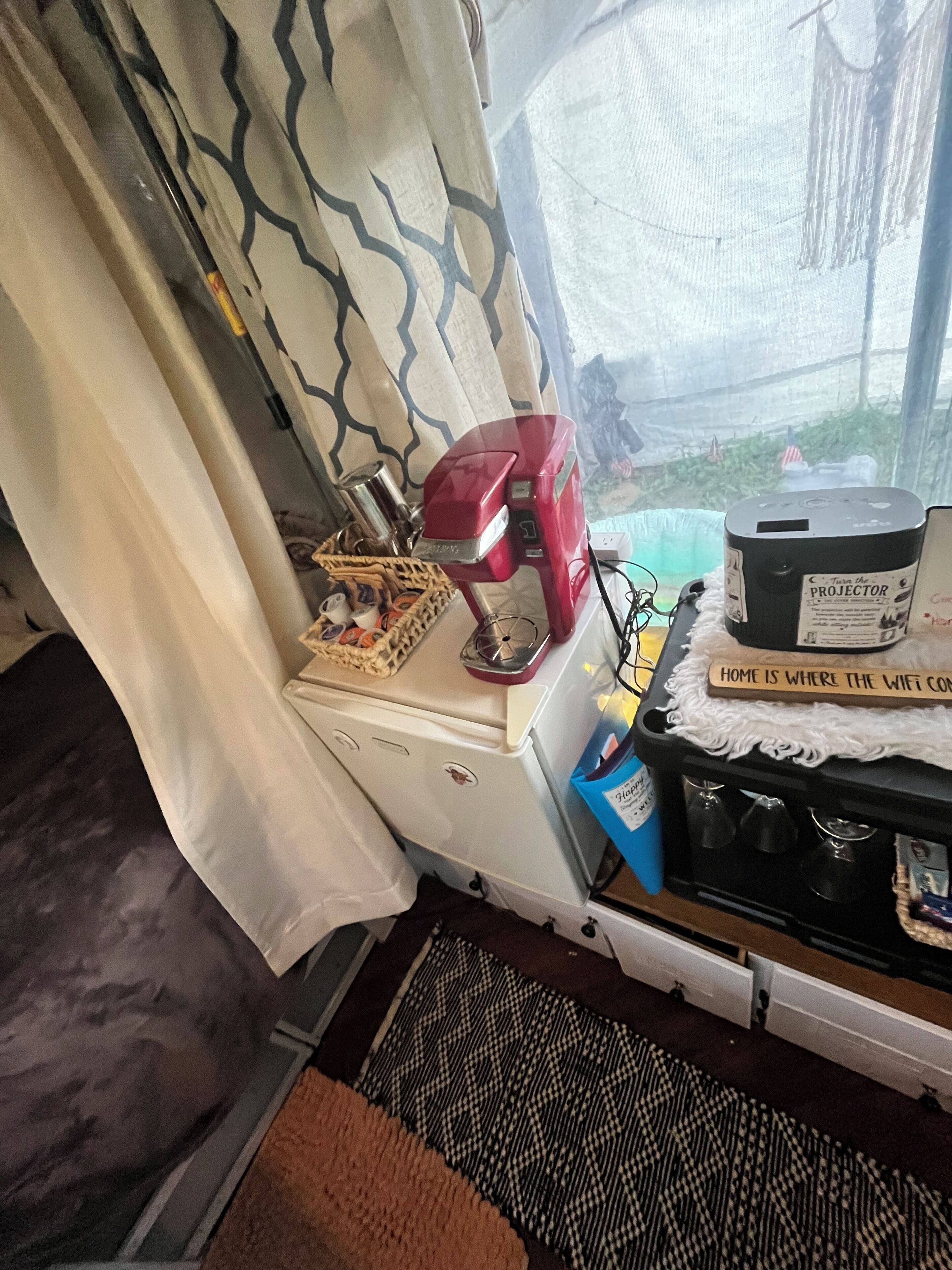 Una habitación con kitchenette, una ventana que da a zonas verdes y una pequeña mesa con un electrodoméstico rojo.