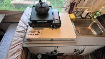 Een kleine keuken met kookplaat, spoelbak en een raam met uitzicht op groen.