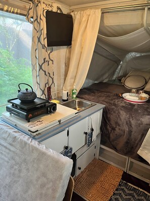 Une tente compacte et bien aménagée, dotée d’un coin cuisine, d’un lit et d’une fenêtre avec des rideaux.