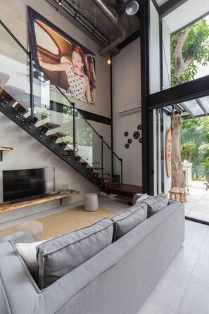 A modern interior with a staircase, a flat-screen TV, and a grey sofa.