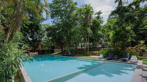 Una piscina rodeada de abundante vegetación y algunas sillas de descanso.