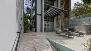 Un edificio moderno con fachada de vidrio, zona de estar al aire libre y una piscina pequeña.