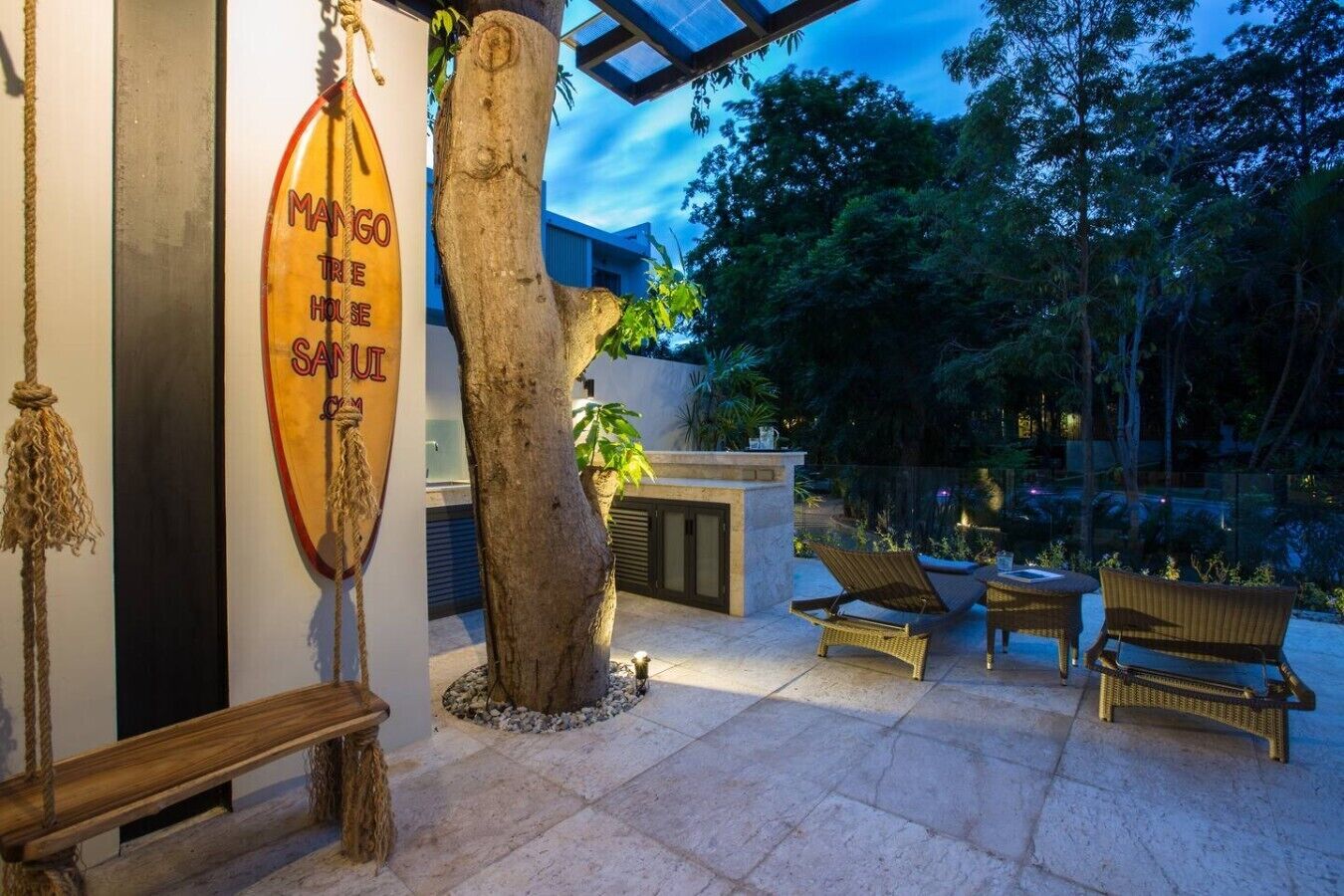A patio area with a tree, wicker furniture, and a sign reading 'MANGO TREE HOUSE SAUI'.