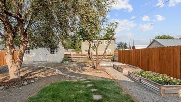 A fenced backyard with a tree, a white building, and a wooden fence.