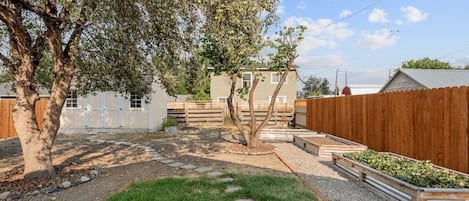 Un patio trasero cercado con un árbol, un edificio blanco y una valla de madera.