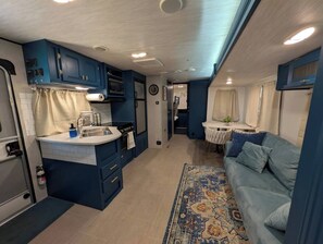 Een compact interieur van een camper met een kitchenette, een eethoek en een zithoek.