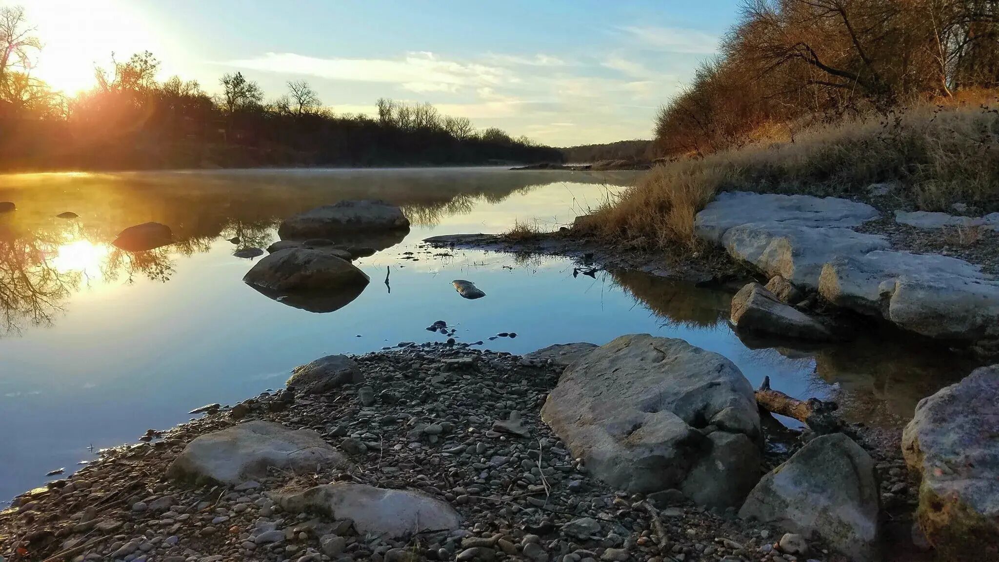 A calm river with rocks and a clear sky.
