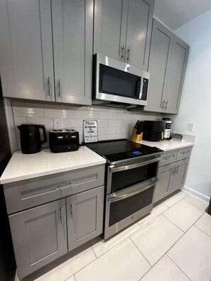 A modern kitchen with grey cabinets, a stainless steel microwave, a coffee maker, and a sign prohibiting smoking or vaping. - Spacious 5-bedroom house in charming Kissimmee with AC (Kissimmee)