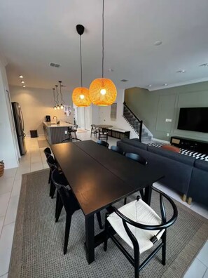 A modern living room with a dark wooden dining table, black chairs, and a large grey sectional sofa. There are two hanging pendant lights with a woven design. - Spacious 5-bedroom house in charming Kissimmee with AC (Kissimmee)