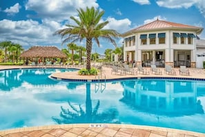 A swimming pool with lounge chairs, a palm tree, and a building with a thatched roof. - Spacious 5-bedroom house in charming Kissimmee with AC (Kissimmee)
