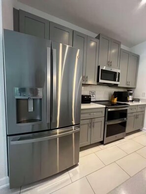 A modern kitchen with stainless steel appliances, grey cabinets, and a tiled floor. - Spacious 5-bedroom house in charming Kissimmee with AC (Kissimmee)