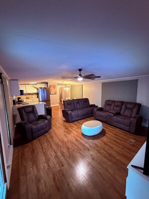 A living room with a sectional sofa, a small ottoman, and a ceiling fan. - Gorgeous 3-bedroom mobile home with AC in Canyon Lake (Canyon Lake)