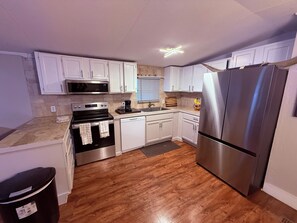 A compact kitchen with white cabinets, a stainless steel refrigerator, a microwave, an oven, and a dishwasher. - Gorgeous 3-bedroom mobile home with AC in Canyon Lake (Canyon Lake)