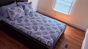Une chambre à coucher avec un lit, un ventilateur de plafond, une fenêtre avec des stores et un plancher en bois.