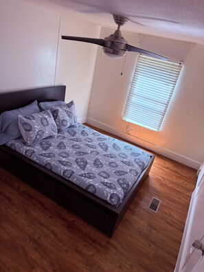 A bedroom with a bed, ceiling fan, window with blinds, and wooden flooring. - Gorgeous 3-bedroom mobile home with AC in Canyon Lake (Canyon Lake)