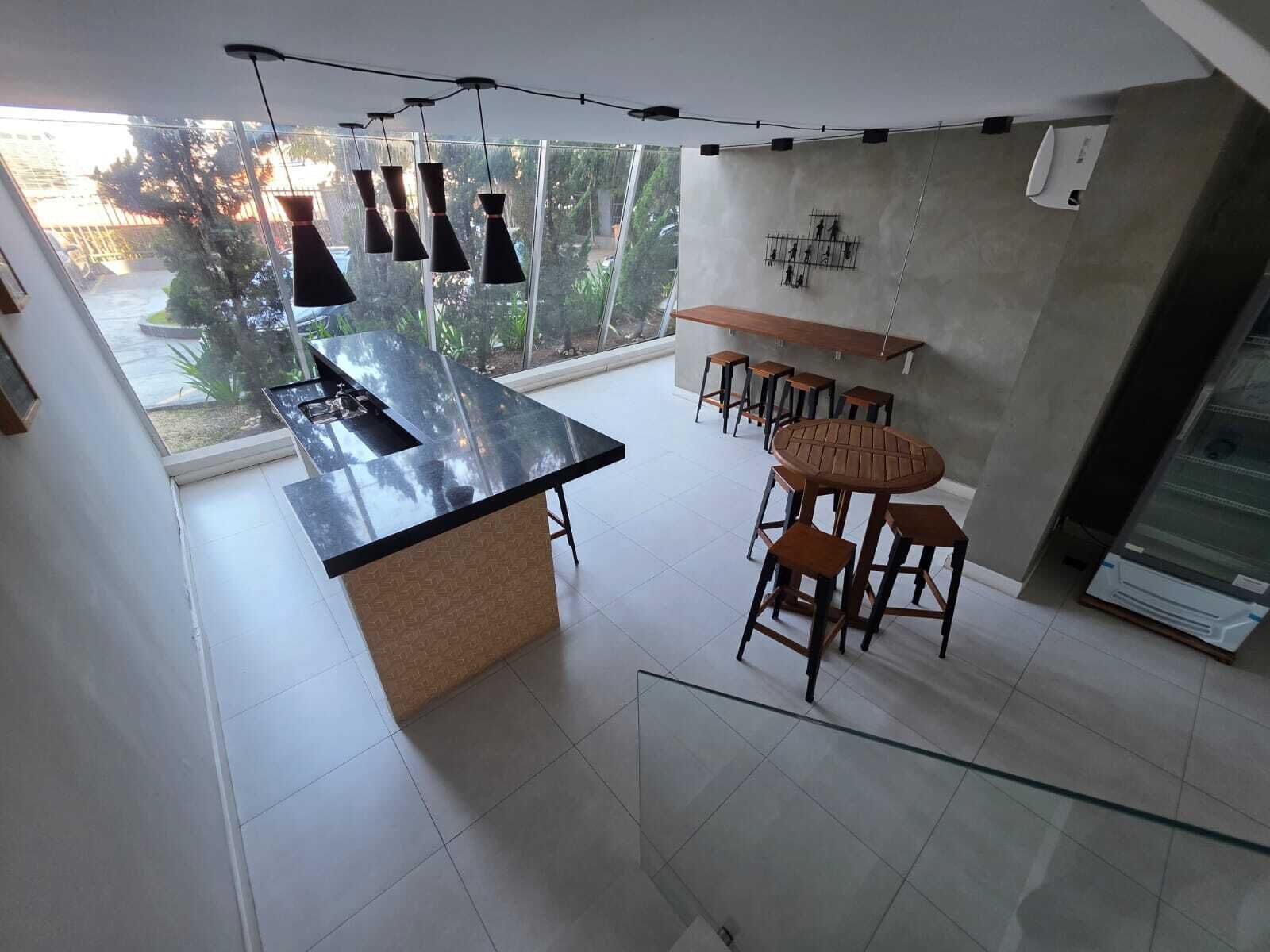 Uma cozinha moderna com uma ilha central, banquetas de bar, luminárias pendentes e vista para o verde lá fora.
