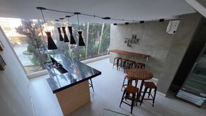 A modern kitchen with a central island, bar stools, pendant lighting, and a view of greenery outside. - Duplex Apartment: Style and comfort just a few meters from Berrini & Shopping (São Paulo)