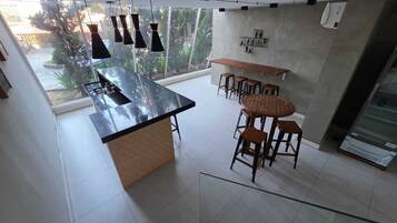 Uma cozinha moderna com uma ilha central, banquetas de bar, luminárias pendentes e vista para o verde lá fora.
