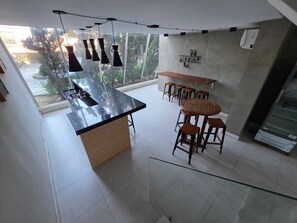 A modern kitchen with a central island, bar stools, pendant lighting, and a view of greenery outside. - Duplex Apartment: Style and comfort just a few meters from Berrini & Shopping (São Paulo)