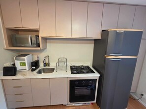A compact kitchen with a microwave, toaster, sink, gas stove, and a refrigerator. - Duplex Apartment: Style and comfort just a few meters from Berrini & Shopping (São Paulo)
