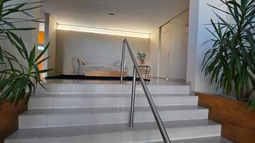 Uma escadaria com corrimão de metal que leva a um quarto com cama e mesa de cabeceira.