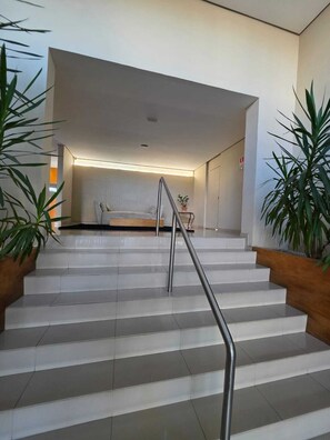 A staircase with a metal handrail leading to a room with a bed and a bedside table. - Duplex Apartment: Style and comfort just a few meters from Berrini & Shopping (São Paulo)
