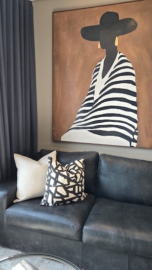 A black leather sofa with two patterned cushions, a large abstract painting, and dark curtains. -  Luxurious and Modern, Menlyn Maine Residences 825, Pretoria (Pretoria)