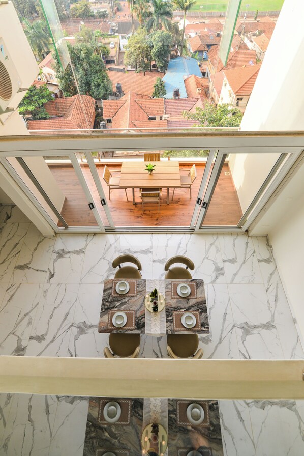 A balcony with a table and chairs, overlooking a residential area with red-tiled roofs.