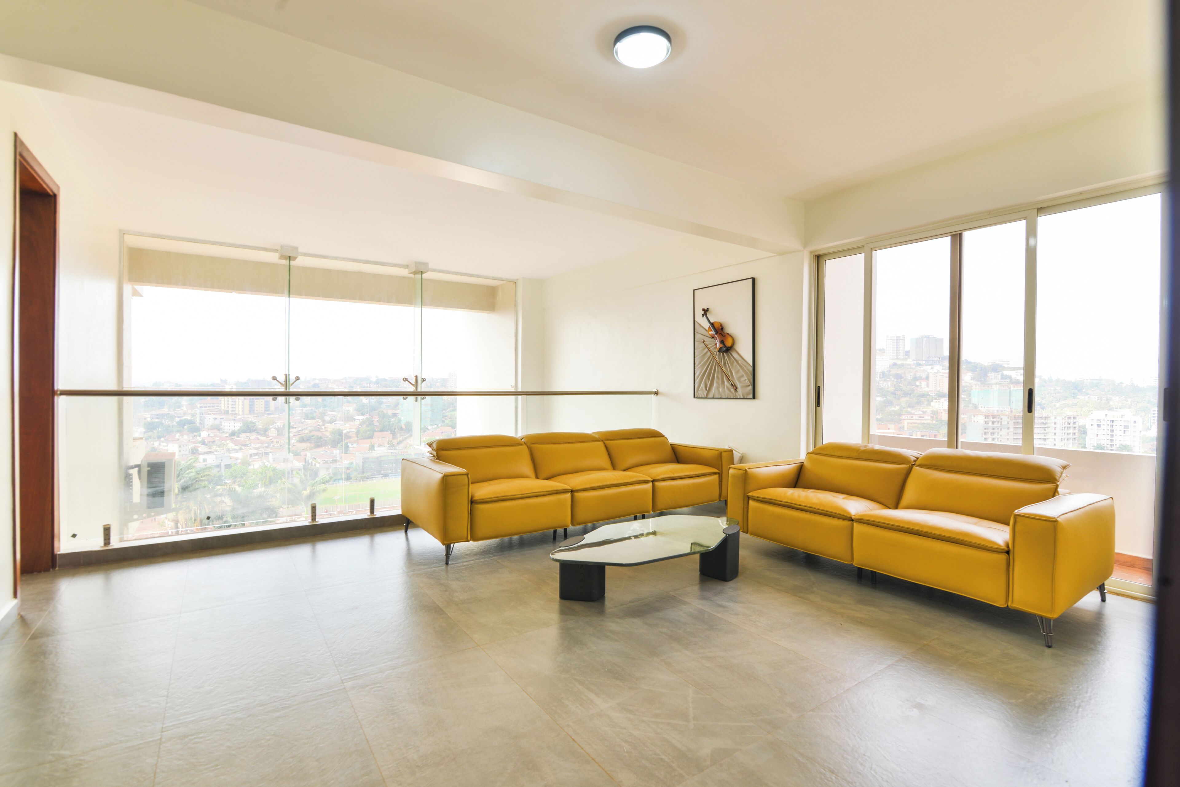 Un salon spacieux avec une grande fenêtre, un canapé jaune et un tableau encadré accroché au mur.