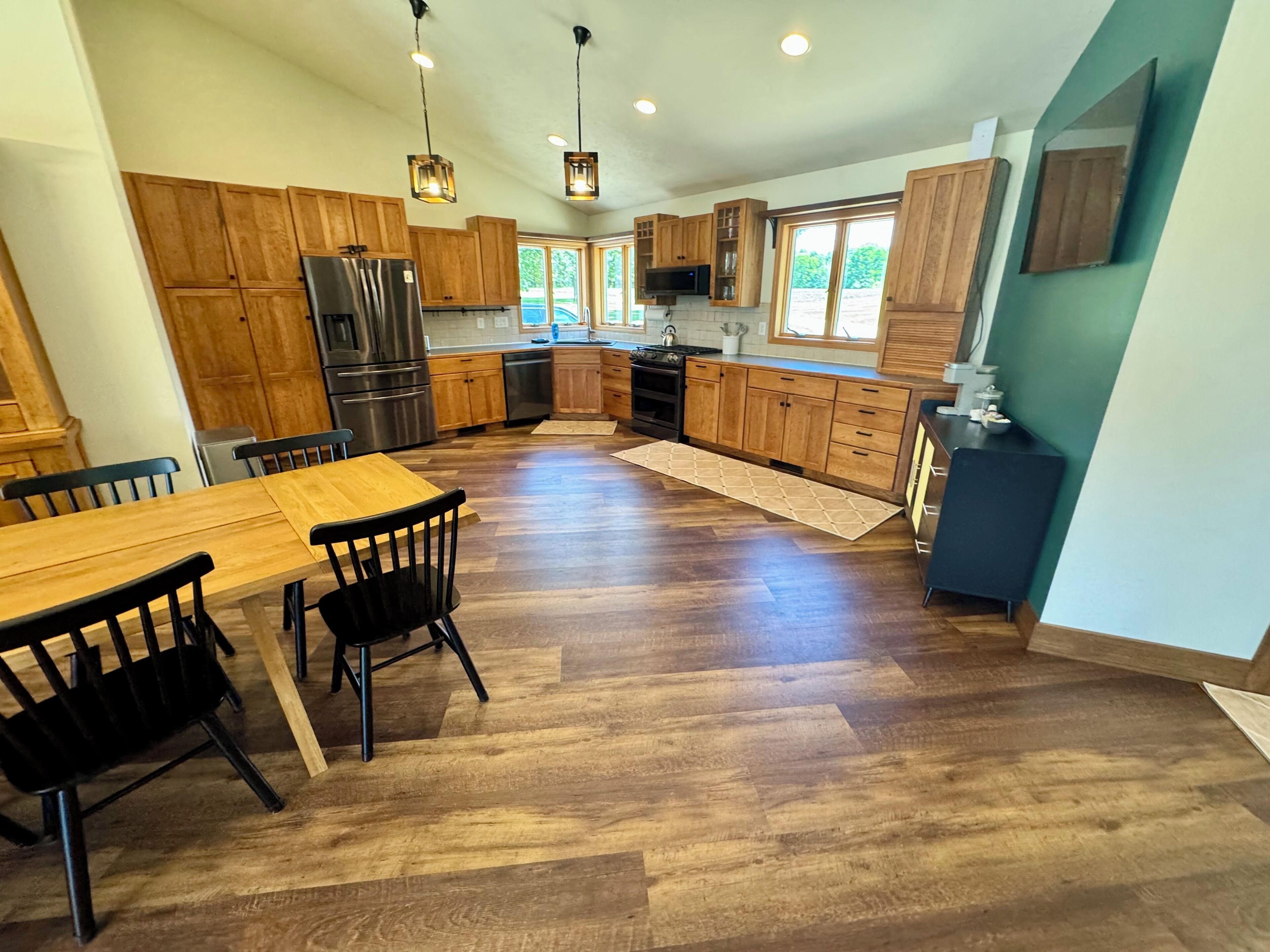 Una cocina moderna con armarios de madera, un refrigerador de acero inoxidable y una zona de comedor con una mesa y sillas de madera.