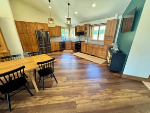 A modern kitchen with wooden cabinets, a stainless steel refrigerator, and a dining area with a wooden table and chairs.