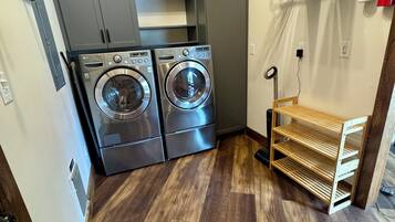 A laundry room with two front-loading washers, a drying rack, and a fire extinguisher.