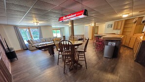 A spacious living area with a wooden dining table and chairs, a sofa, and a kitchen area with wooden cabinets and a refrigerator.