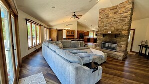 A spacious living room with a large sectional sofa, a fireplace, and a kitchen in the background.