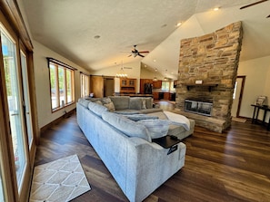 A spacious living room with a large sectional sofa, a fireplace, and a kitchen in the background.