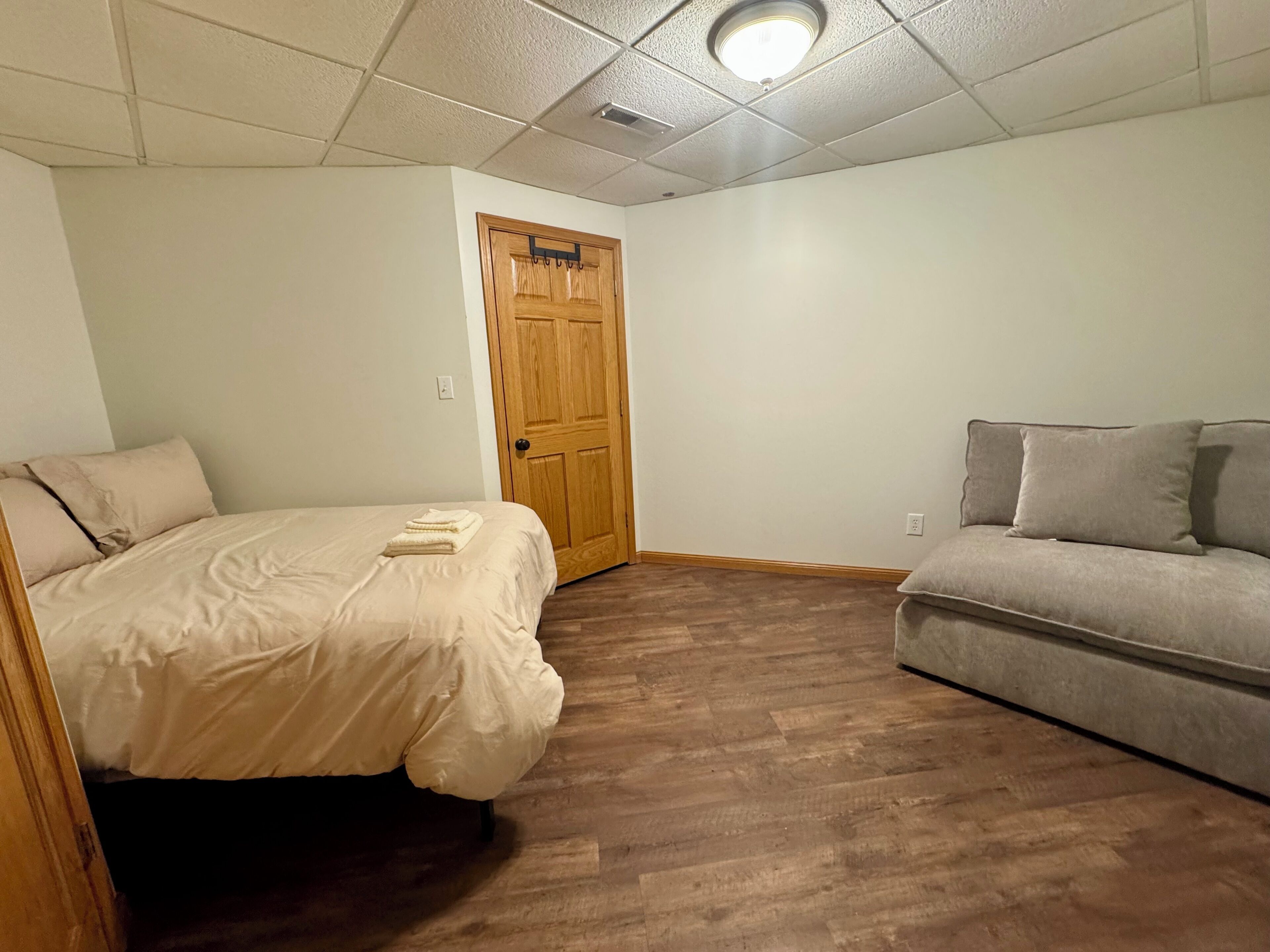 Una habitación con cama, sofá, puerta de madera y una lámpara en el techo.