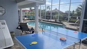 Un tavolo da ping pong con una rete, sedie e una piscina sullo sfondo.