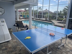 Ein Tischtennis-Tisch mit Netz, Stühle und ein Schwimmbecken im Hintergrund.