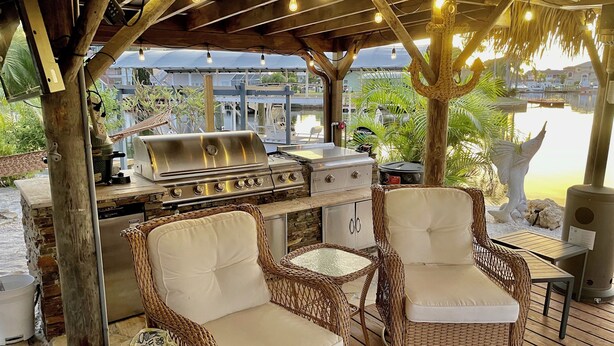 Patio esterno con barbecue, mobili in vimini e vista su un corpo d'acqua.