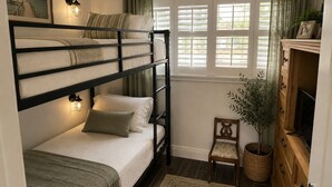 Camera con letto a castello, finestra, una sedia, una pianta e un televisore.