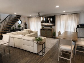 Ein modernes Wohnzimmer mit einer Eckcouch, einem Esstisch mit Stühlen, einer Treppe und einem Fernseher.