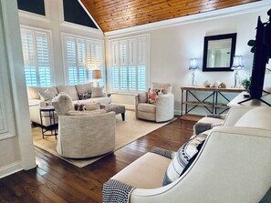 A spacious living room with a high ceiling, large windows, and a variety of seating options including a sofa, armchairs, and a round ottoman. - Panoramic Views of KY Lake.  (Buchanan)