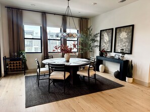 A dining area with a round table, chairs, a vase with flowers, a hanging light fixture, and artwork on the wall. - Ocean View Luxury Condo off Monterey Bay Brand New (Marina)